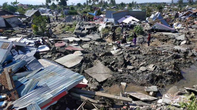 Warga melintas di antara reruntuhan rumah di Perumnas Bala Roa, Palu.