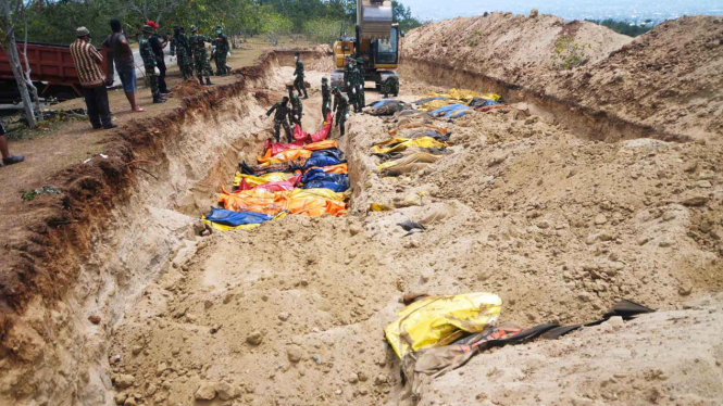 Petugas dengan alat berat mengubur jenazah korban gempa Palu di TPU Poboya Indah, Palu, Sulawesi Tengah