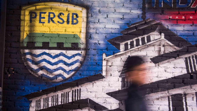 Bobotoh alias pendukung Persib berjalan di depan mural Persib di Bandung, Jawa Barat