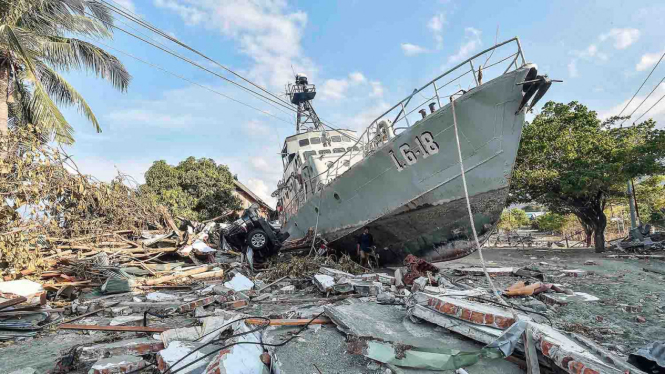 Warga berada di dekat kapal TNI AL yang terdampar di jalanan akibat tsunami.