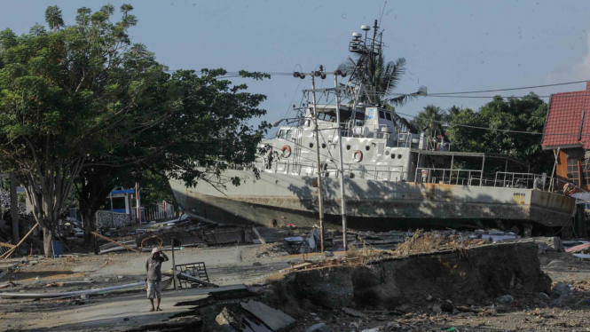 Warga melintas di dekat kapal TNI AL yang terdampar di jalanan akibat tsunami di Watusampu, Ulujadi, Palu, Sulawesi Tengah, Kamis, 4 Oktober 2018.