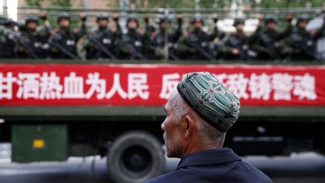 Seorang warga Uighur menyaksikan polisi militer dalam parade anti teror di China.