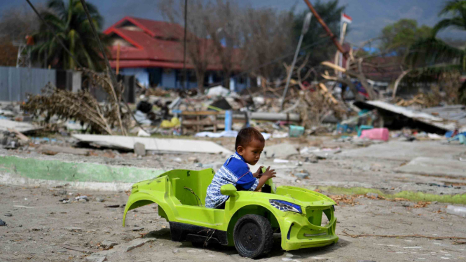 Seorang anak bermain mainan mobil yang rusak pascagempa dan tsunami Palu di Pantai Talise, Palu, Sulawesi Tengah