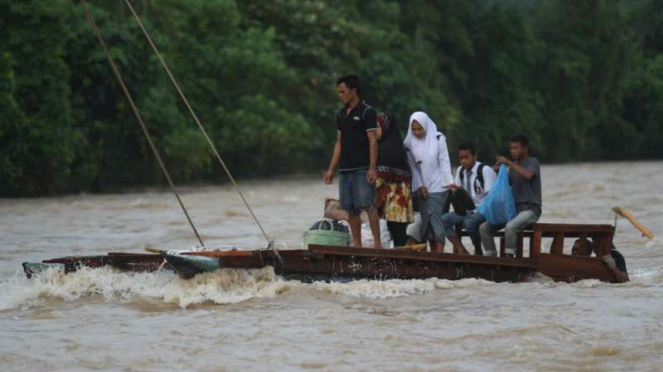 Masyarakat korban banjir, terutama para pelajar, di Kabupaten Pasaman Barat, Sumatera Barat, menyeberangi sungai yang arusnya deras dengan rakit darurat untuk ke sekolah pada Rabu, 17 Oktober 2018.