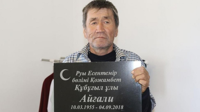 Esengali Supygaliev memegang batu nisan kakaknya Aigali di Kazakhstan. - Azh.kz