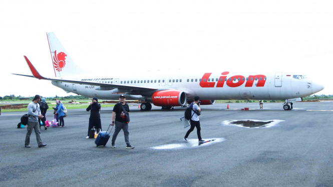 Penumpang berjalan di samping pesawat Lion Air jenis Boeing 737-900 ER.