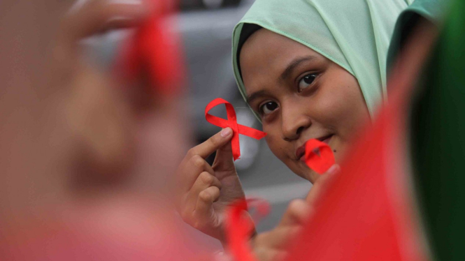 Mahasiswi Universitas Bhayangkara Surabaya menunjukkan pita merah yang akan dibagikan kepada pengguna jalan saat melakukan aksi peringatan Hari AIDS Sedunia di Surabaya, Jawa Timur