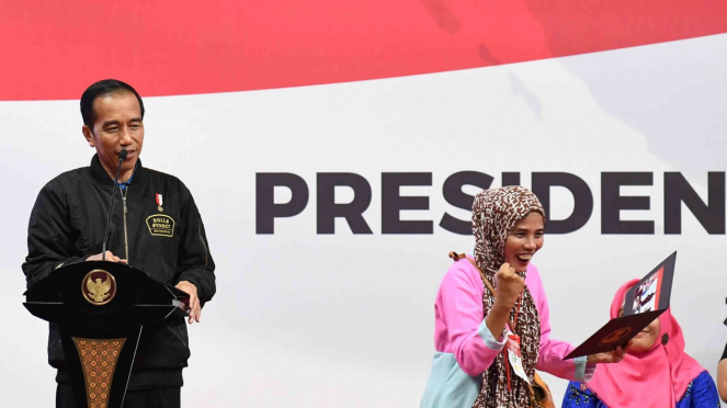 Presiden Joko Widodo (kiri) memberikan foto kepada penerima kartu Program Keluarga Harapan (PKH) saat sosialisasi di Gelanggang Remaja Jakarta Timur, Jakarta.