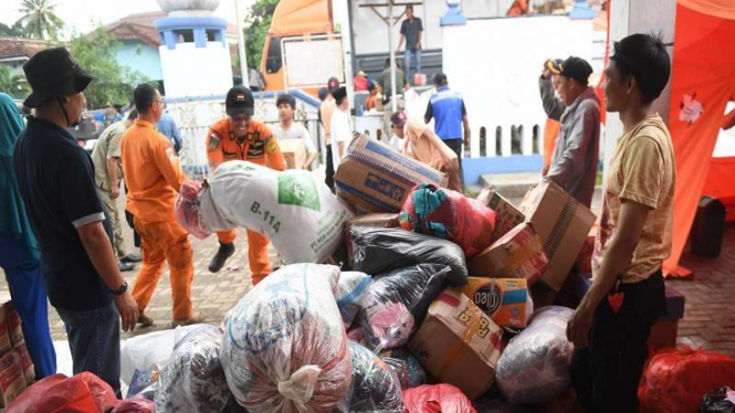 Warga bersama relawan menurunkan bantuan yang tiba untuk pengungsi tsunami