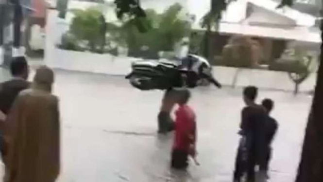 Pria panggul sepeda motor melintasi banjir.