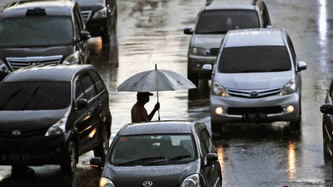 Warga menyeberang menggunakan payung saat hujan di Jakarta 