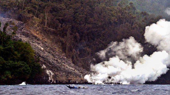 Sejumlah anggota polisi yang mengangkut bantuan logistik dengan perahu motor melintas di dekat lokasi guguran material vulkanik Gunung Karangetang di Pulau Siau, Kabupaten Kepulauan Sitaro, Sulawesi Utara