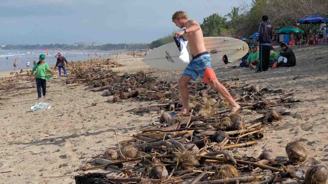 Wisatawan mancanegara melintas di atas sampah yang terdampar akibat cuaca buruk di Pantai Kuta, Badung, Bali, Senin, 11 Februari 2019.