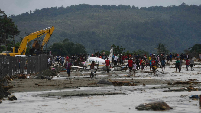 Warga mengamati sebuah pesawat yang terseret banjir bandang di Sentani, Jaya Pura, Papua, Senin, 18 Maret 2019.