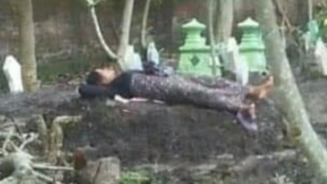 Seorang ibu tidur di makam anaknya.
