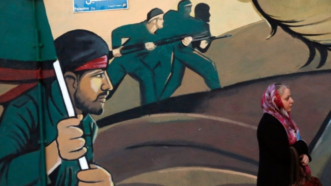 Seorang perempuan berjalan melintasi mural di Teheran yang menggambarkan para prajurit Iran.-EPA