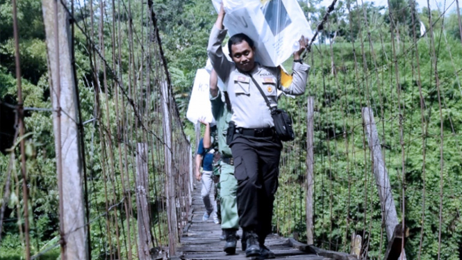 Bripka Suryadi saat melewati jembatan gantung dengan konstruksi seadanya, untuk mendistribusikan logistik ke TPS terpecil di tempat ia bertugas (FOTO: Istimewa)