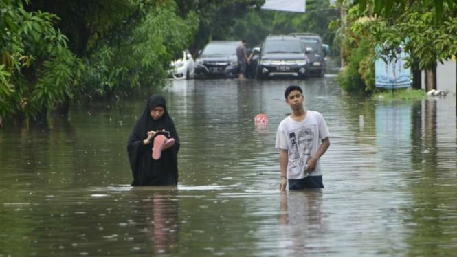 Warga Rawalumbu, Kota Bekasi, Jawa Barat, berusaha menerobos genangan banjir akibat hujan deras dan lama pada Rabu, 24 April 2019.