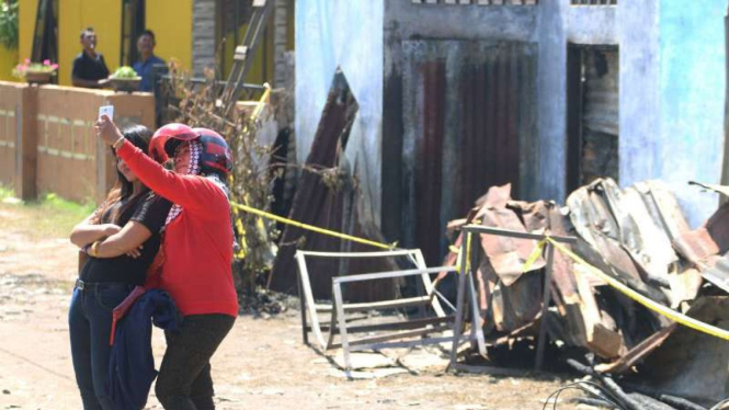 Dua wanita berswafoto dengan latar belakang bangunan pabrik korek api gas (mancis) yang hangus terbakar, di Desa Sambirejo, Langkat, Sumatera Utara, Minggu, 23 Juni 2019. 