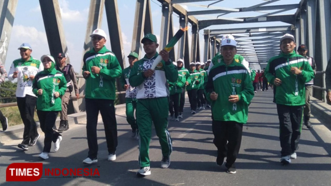 Atlet berprestasi Kabupaten Tuban didampingi Ketua Umum KONI Tuban, Sekda Tuban dan Komandan Kontingen Tuban saat membawa Api Porprov VI Jawa Timur di jembatan Glendeng, Soko, Tuban, Selasa, (02/07/2019). (FOTO: Achmad Choirudin/TIMES Indonesia)