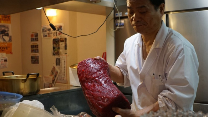 Seorang koki di restoran daging paus di Tokyo menunjukkan potongan daging merah. - Getty Images