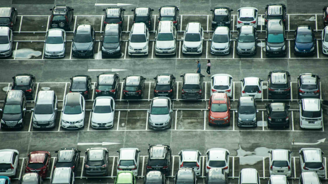 La población está caminando en Yakarta entre autos estacionados.