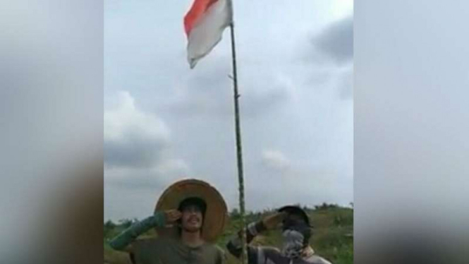 TKI mengibarkan bendera merah putih di tengah lahan sawit di Malaysia.