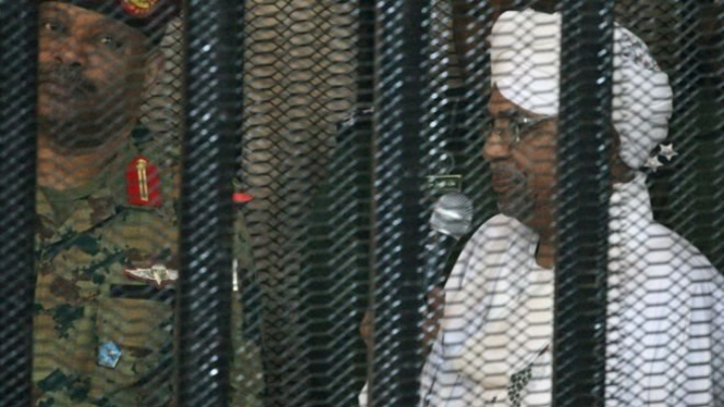 Omar al-Bashir muncul di pengadilan di balik sel pada hari Senin. - AFP.