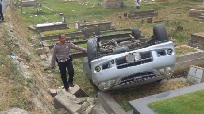 Polisi memeriksa sebuah mobil yang timpa makam di TPU Tanah Kusir