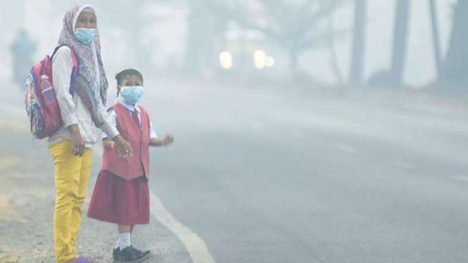 Seorang siswa bersama orang tuanya mengenakan masker saat menunggu angkutan umum, di Palembang, Sumatera Selatan, Senin (23/9/2019). Pemerintah Kota Palembang meliburkan siswa sekolah selama tiga hari, 23-25 September 2019 akibat kabut asap. 