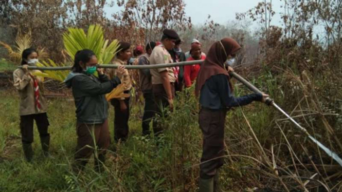 Sejumlah siswa Pramuka membantu petugas memadamkan kebakaran hutan dan lahan gambut di kawasan Rimbo Panjang, perbatasan Pekanbaru dengan Kabupaten Kampar, Riau, Selasa, 24 September 2019.