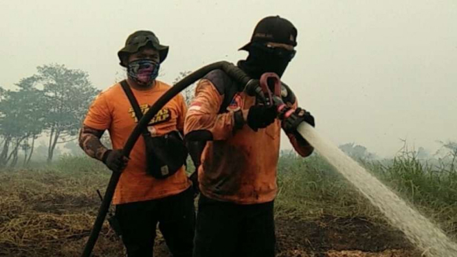 Dua petugas menyemprotkan air untuk memadamkan kebakaran hutan dan lahan gambut di wilayah Rantau Bakung, Kecamatan Rengat Barat, Kabupaten Indragiri Hulu, Riau.