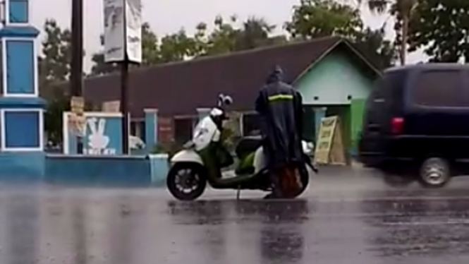 Pemotor mengenakan jas hujan di tengah jalan.