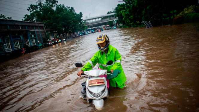 Warga mendorong motor lintasi banjir di Jalan DI Panjaitan, Cawang, Jakarta Timur.