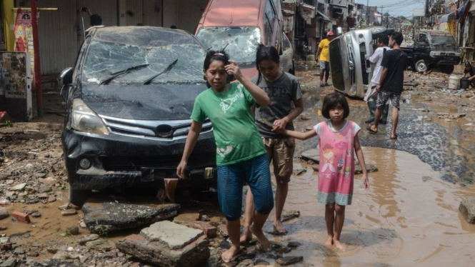 Sejumlah warga berjalan di dekat mobil yang rusak pascabanjir di Perumahan Pondok Gede Permai Bekasi, Jawa Barat, Kamis (02/01) - ANTARA