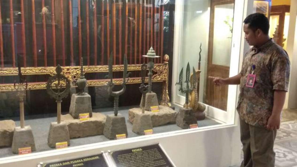  A museum curator points at a display case containing various pusaka kerajaan (heirlooms) of the Indonesian kerajaan (kingdoms).