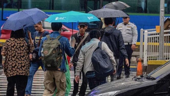 Warga berjalan menggunakan payung saat turun hujan di Jakarta.