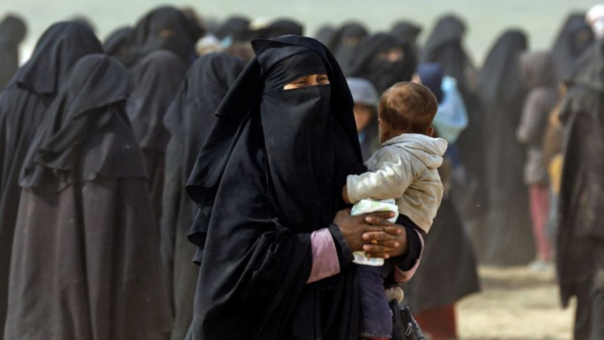 Seorang wanita berkerudung penuh menggendong bayinya melarikan diri dari kelompok Negara Islam di Baghouz pada 13 Februari 2019 - Getty Images/AFP/DELIL SOULEIMAN