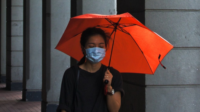 Wanita pakai masker dan payung.