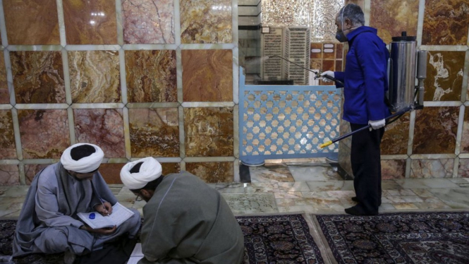 Seorang pria menyemprotkan disinfektan di tempat suci Fatima Masumeh di Iran. - Getty Images