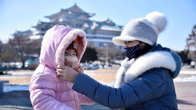Seorang ibu mengenakan masker ke wajah anaknya di Pyongyang - KIM WON-JIN/AFP