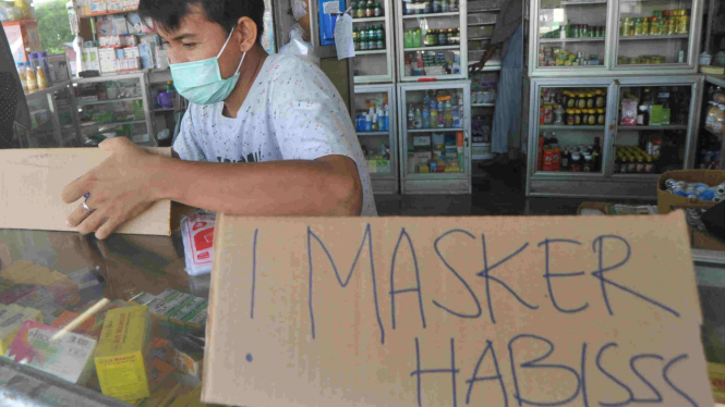 Petugas apotek memasang pengumuman stok masker habis