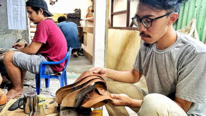 Nurman Farieka (kanan) saat menyulam sepatu dari kulit ceker ayam.