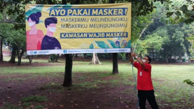 Petugas Taman Margasatwa Ragunan, memasang spanduk sosialisasi memakai masker.
