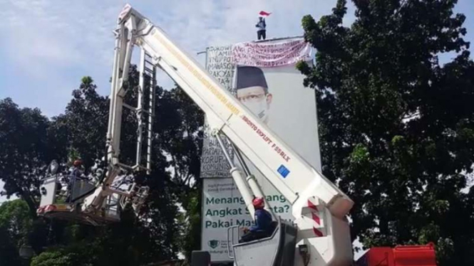 Pria paruh baya naik ke atas papan reklame sambil membentangkan spanduk protes
