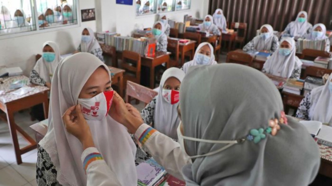 Seorang petugas kesehatan masyarakat menunjukkan kepada siswa cara memakai masker dengan benar di sebuah sekolah di Jakarta.