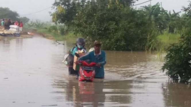 Warga mendorong sepeda motornya di tengah jalan yang tergenang banjir di Kabupat