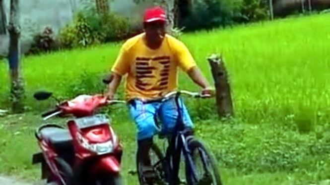 Seorang pria menuntun motor pakai sepeda