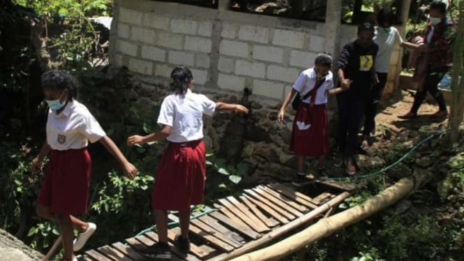 Sejumlah murid dengan hati-hati menyeberangi jembatan darurat ketika hendak berangkat ke sekolah di Kecamatan Alak, Kota Kupang, Nusa Tenggara Timur, Kamis, 18 Maret 2021.