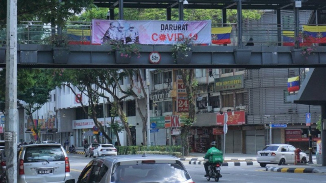 Pengendara lalu lintas melintasi spanduk bertuliskan darurat COVID-19  di Jalan Raja Laut Kuala Lumpur.